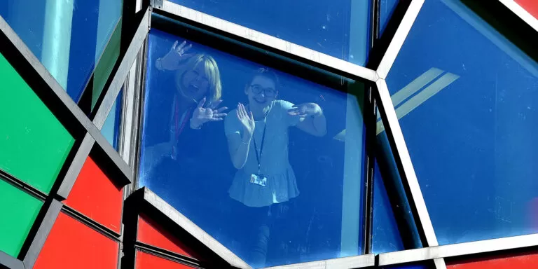 Two women waving through a mosaic-shaped window