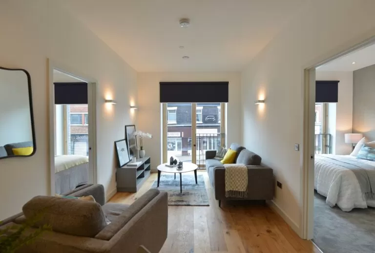Living room with grey sofa, window overlooking highstreet, leading through to bedroom