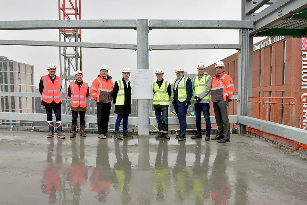 Eight people in high-vis vests stand on a rooftop