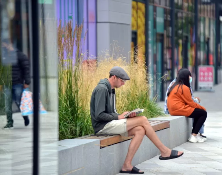 Man sits on a grey and wooden bench reading a book