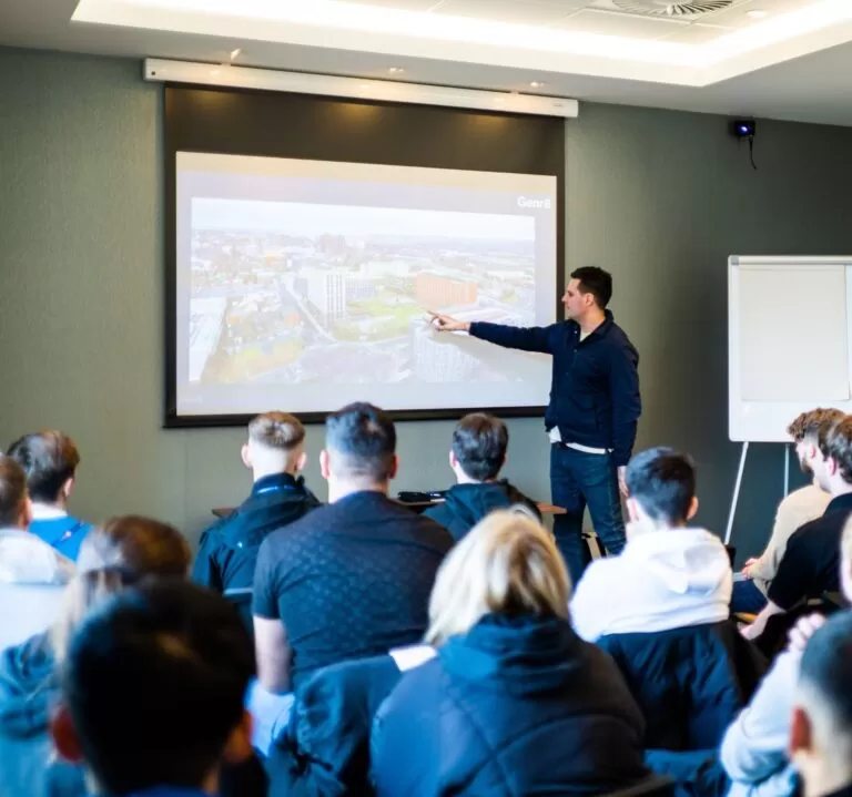 Man pointing at projector screen in front of group of people