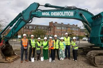 Nine people in hi-vis vests stood beneath a digger